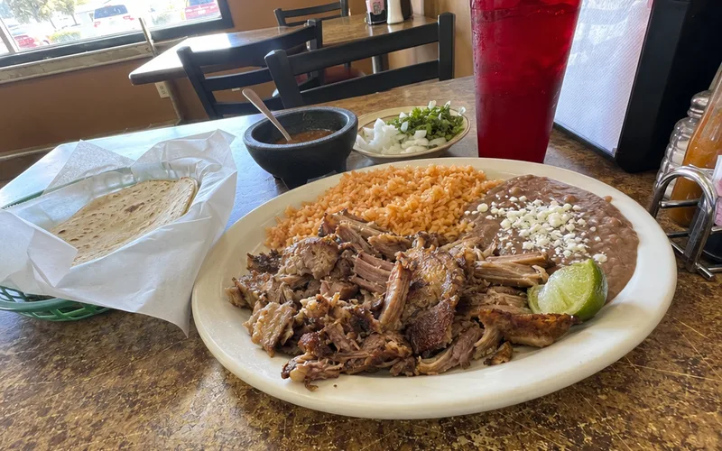 A carnitas plate with rice, beans and tortillas on a family restaurant table
