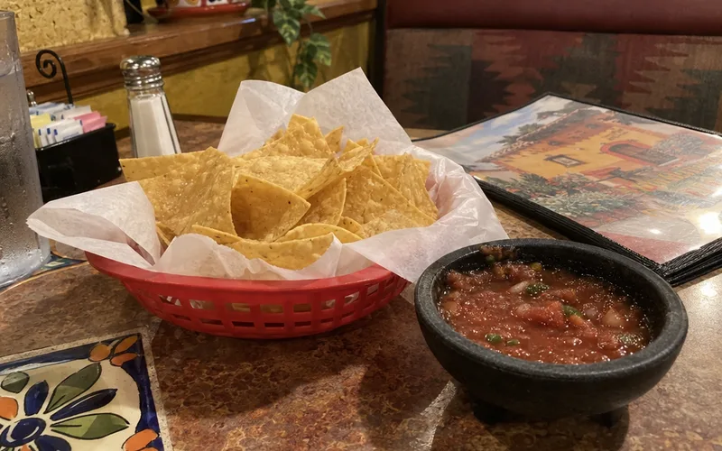 A basket of tortilla chips and a bowl of salsa on a booth table