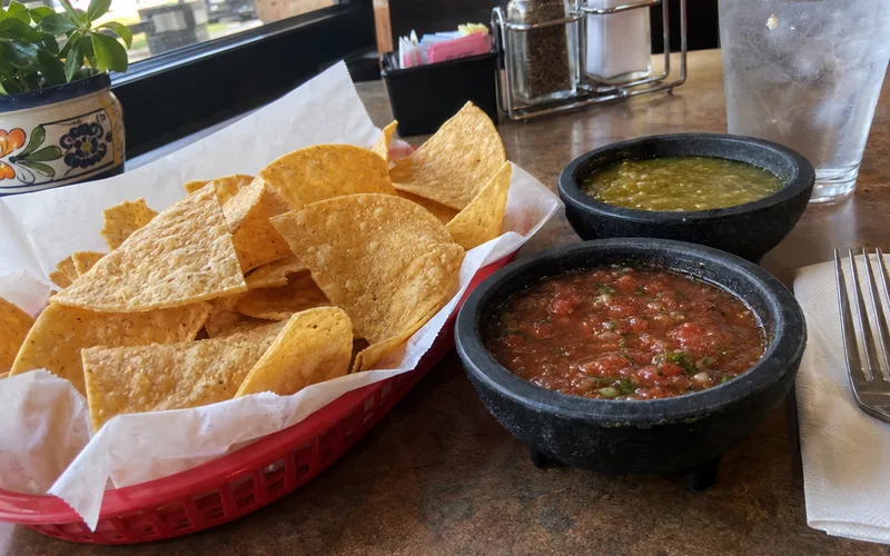 Basket of tortilla chips with red and green salsa on a restaurant table
