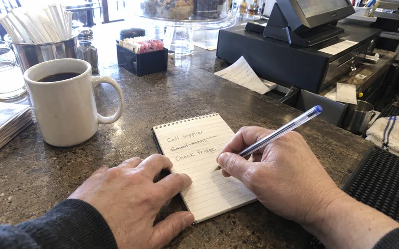Hands writing short notes on a notepad at a restaurant counter