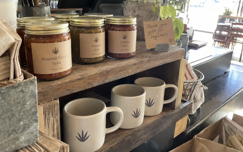 Jars of house-made salsa and logo mugs set aside as customer appreciation gifts