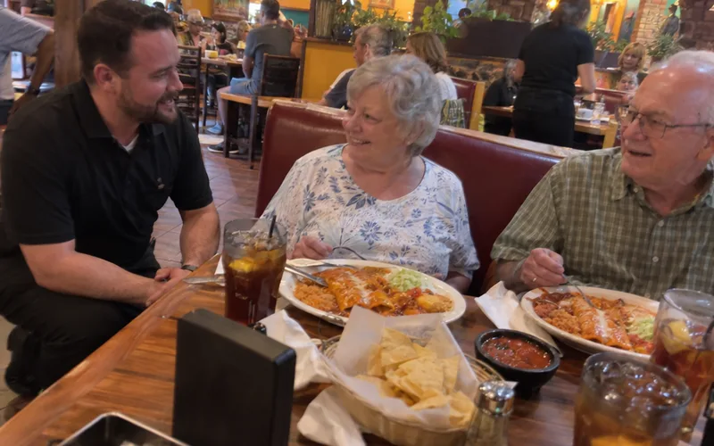 A restaurant manager kneeling beside a booth to check on two guests during their meal