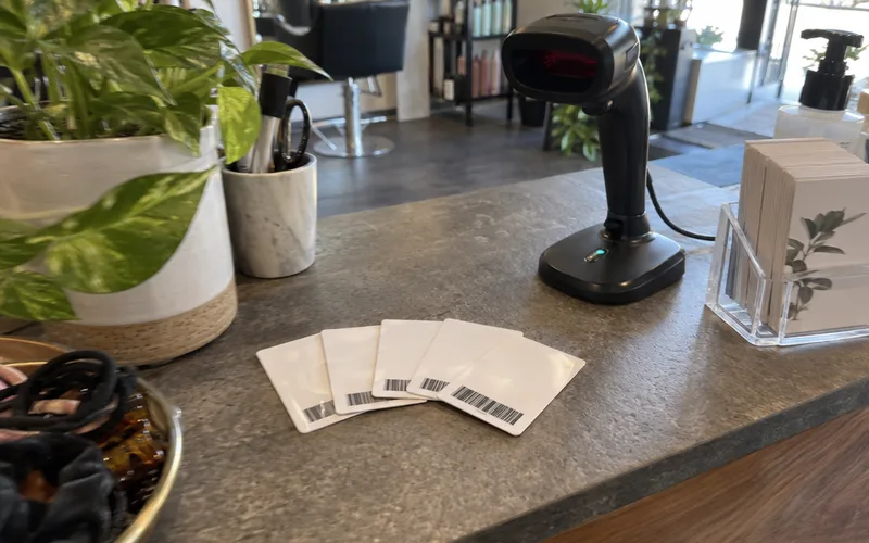 Several plastic loyalty cards with barcodes fanned out next to a handheld barcode scanner on a salon front desk