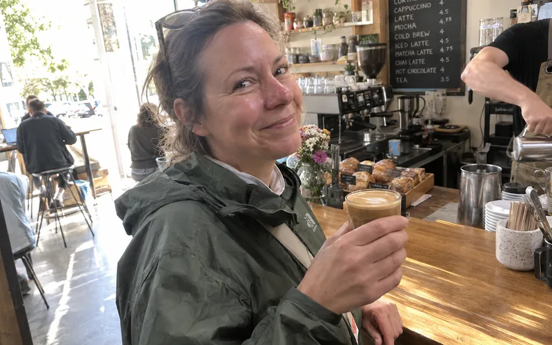 A regular customer holding her usual cortado at a coffee shop counter