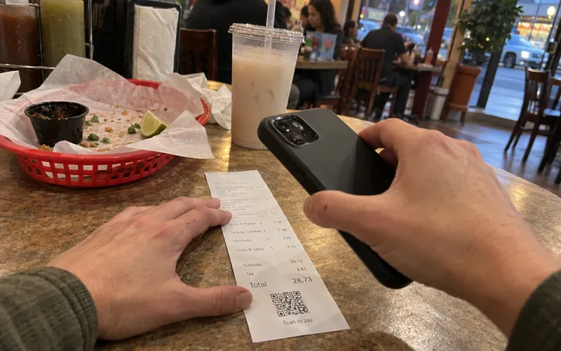 A guest holding a phone over the QR code printed at the bottom of a taqueria receipt