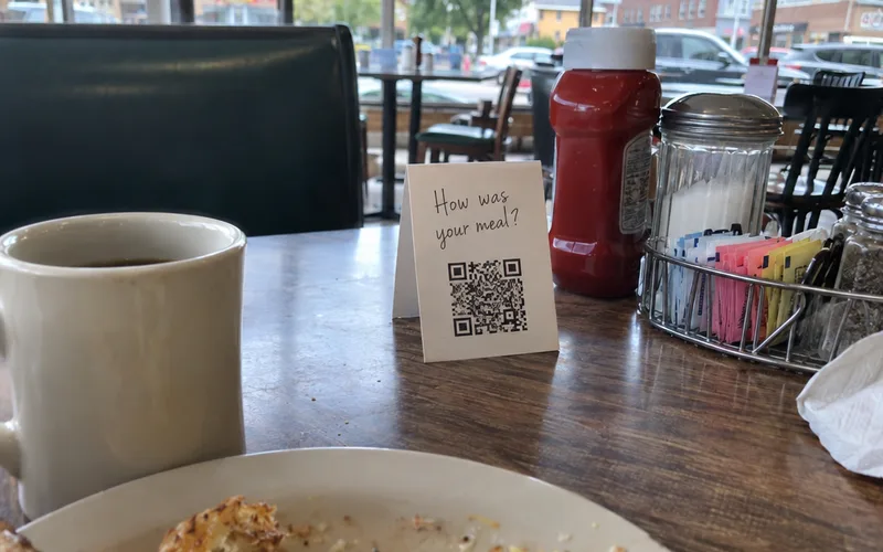 A paper table tent with a QR code on a diner table next to ketchup and a sugar caddy